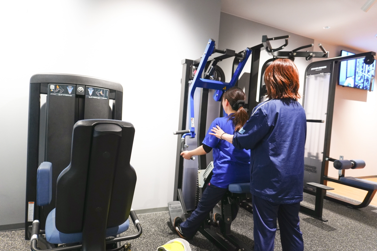 トレーナーに教わりながらマシンを利用する女子学生の様子