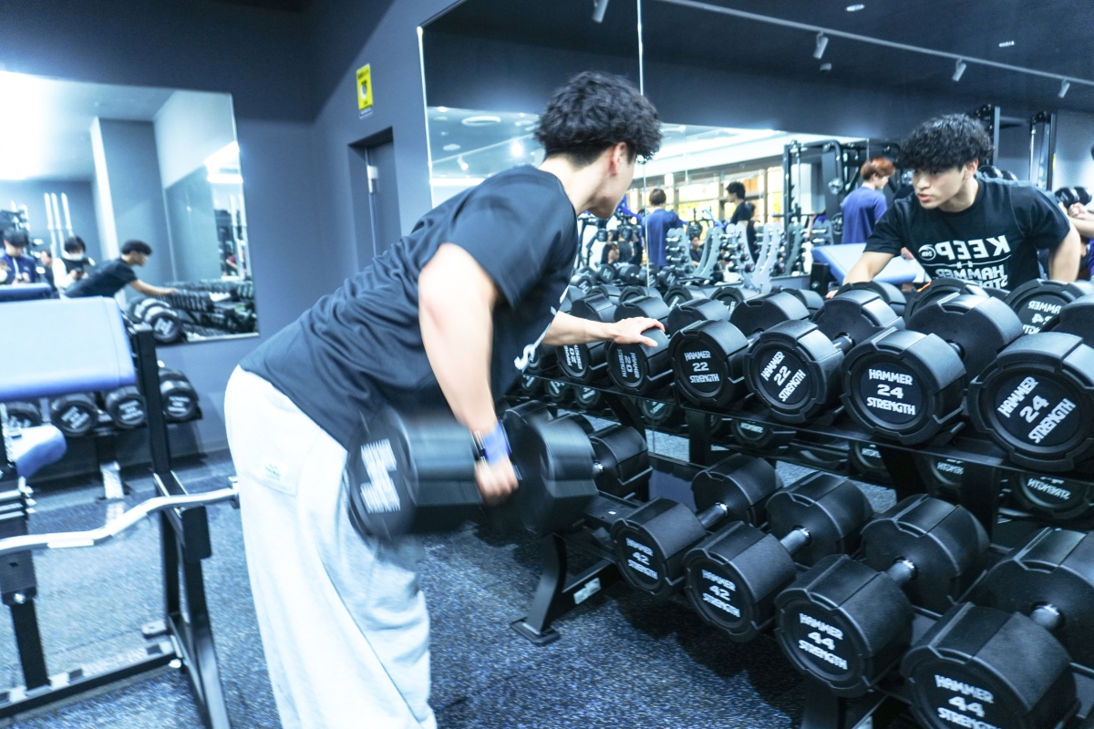 並んだダンベルの前に立ち、真剣な表情で感触を確かめる元山さんの様子