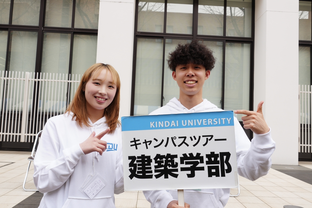 瀧上亜希子さんと西方一樹さんが建築学部のプラカードを笑顔で持っている様子